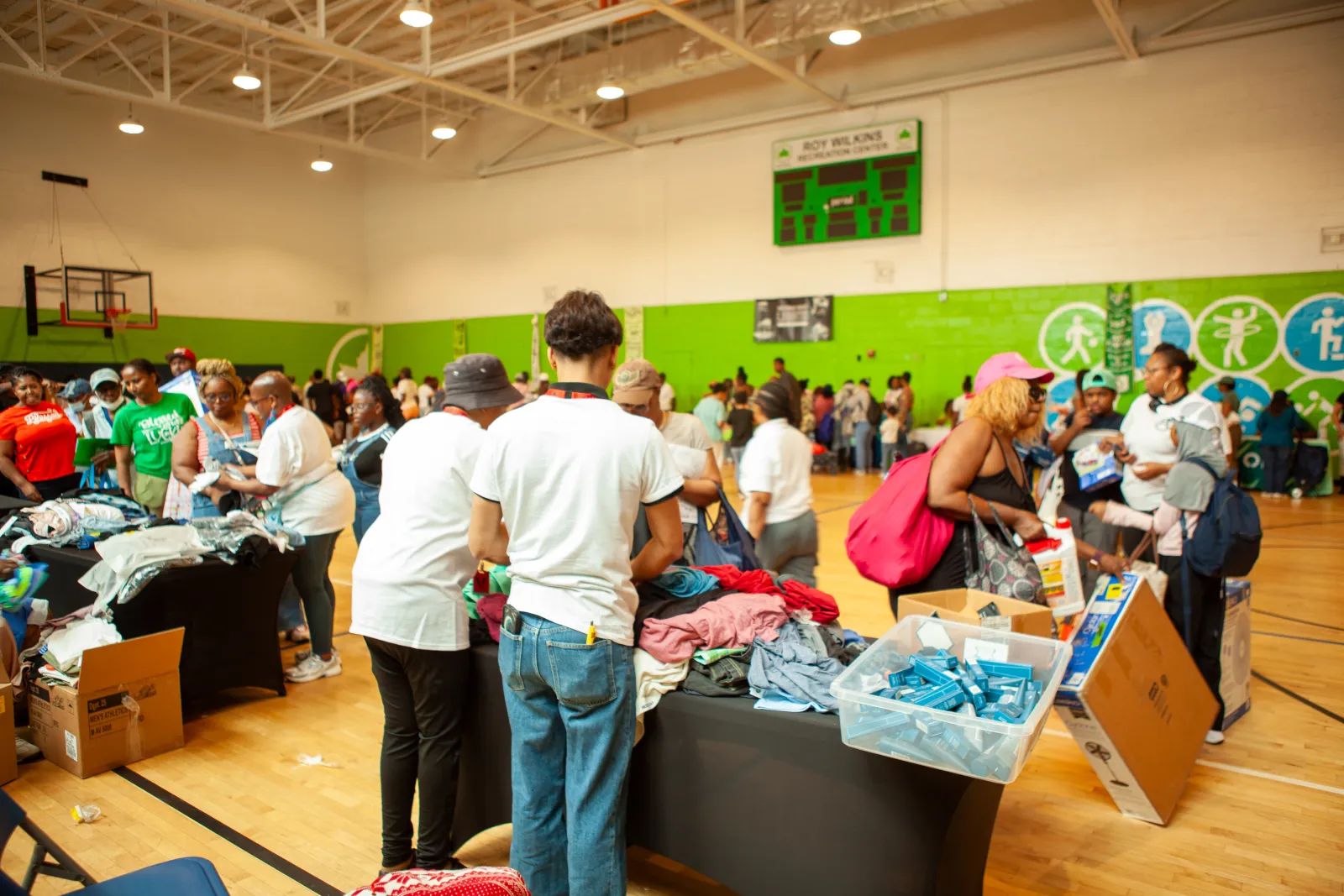 Volunteers and families at a Queens Community Closet distribution event, with tables of free clothing and essentials